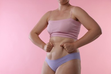 Photo of Liposuction. Woman in underwear touching her belly on pink background, closeup