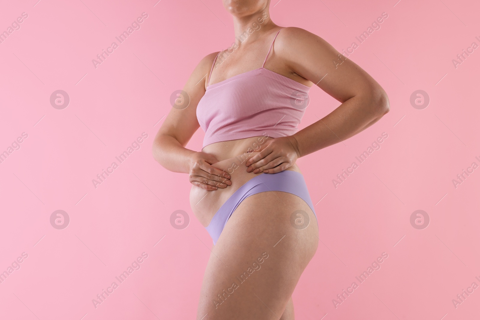 Photo of Liposuction. Woman in underwear touching her belly on pink background, closeup