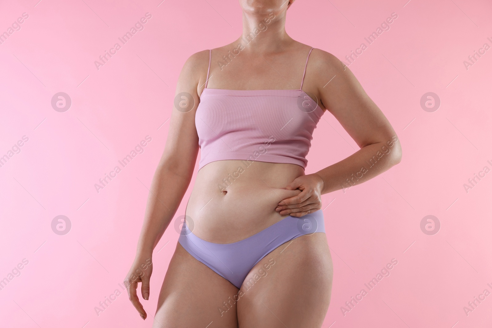Photo of Liposuction. Woman in underwear touching her belly on pink background, closeup