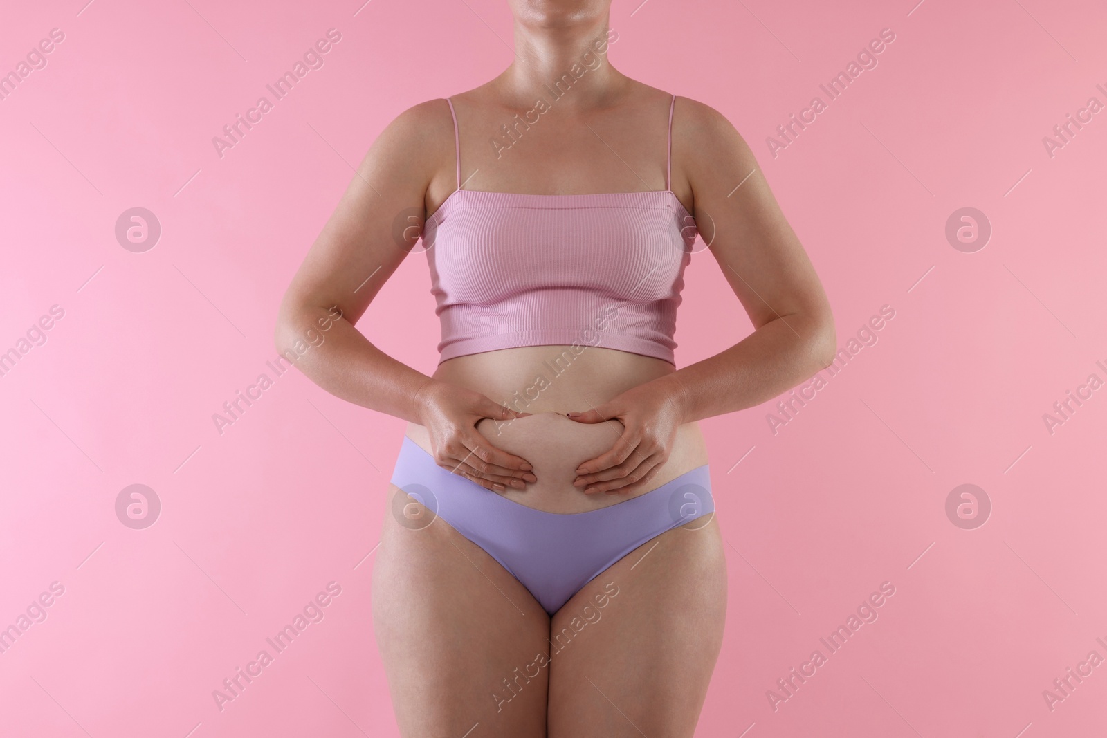 Photo of Liposuction. Woman in underwear touching her belly on pink background, closeup