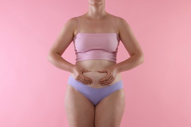 Photo of Liposuction. Woman in underwear touching her belly on pink background, closeup