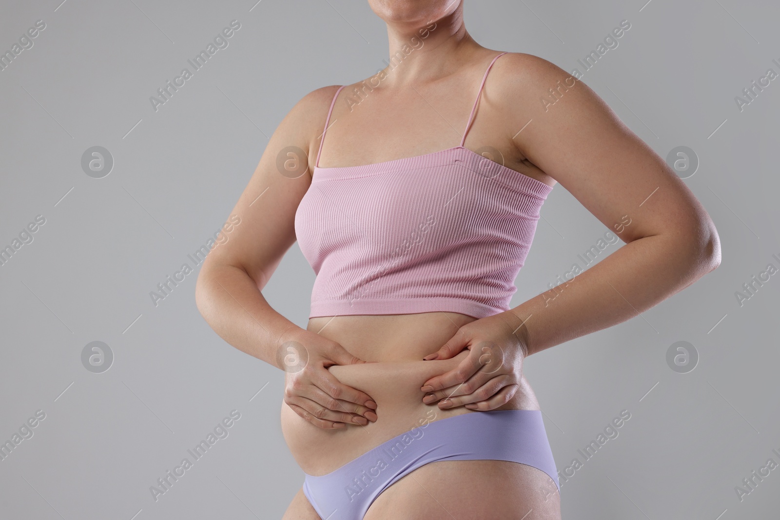 Photo of Liposuction. Woman in underwear touching her belly on grey background, closeup