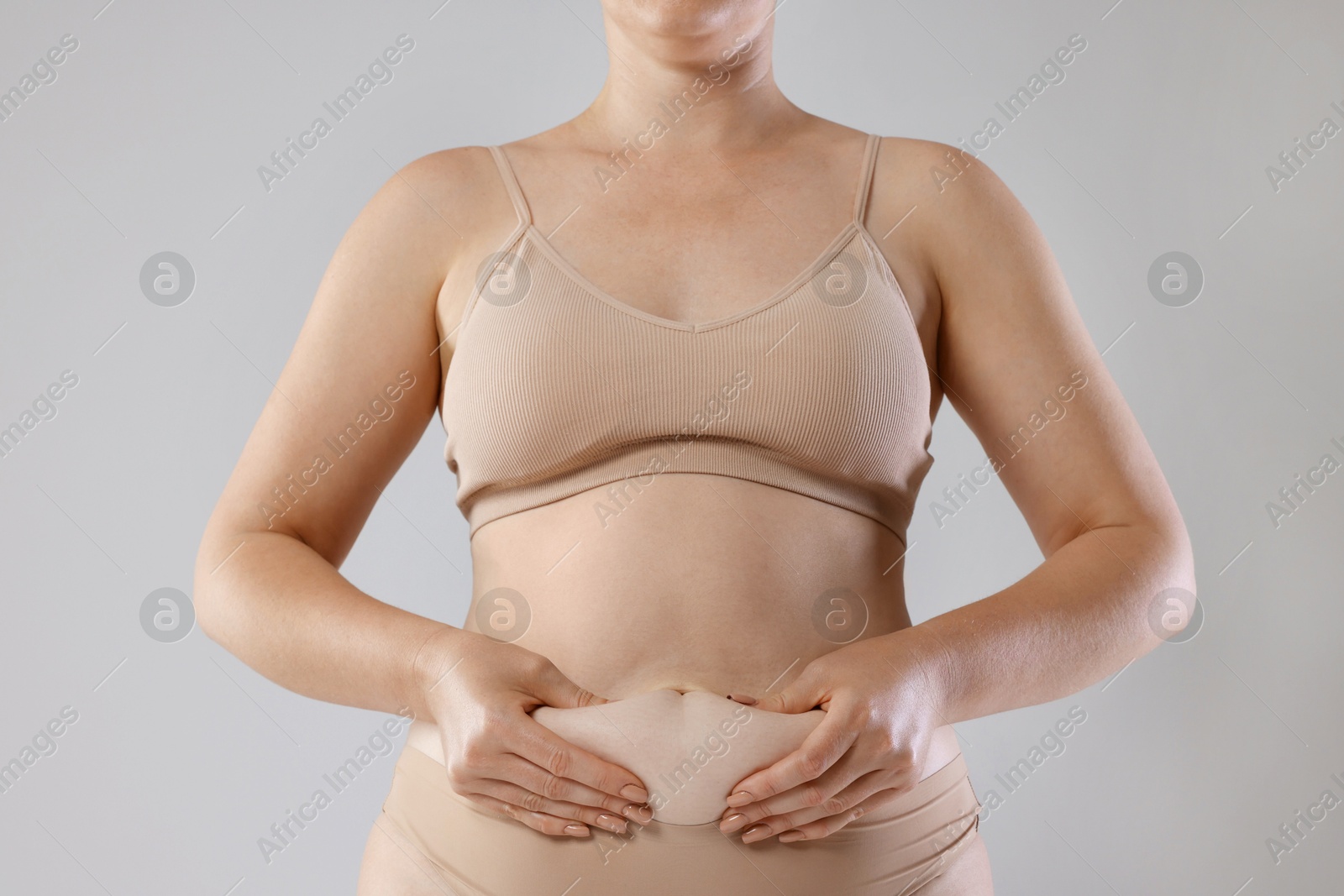Photo of Liposuction. Woman in underwear touching her belly on grey background, closeup