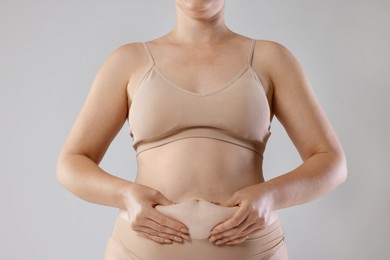 Photo of Liposuction. Woman in underwear touching her belly on grey background, closeup