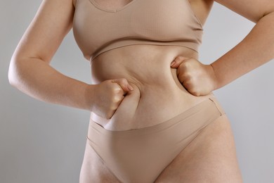 Photo of Liposuction. Woman in underwear touching her belly on grey background, closeup