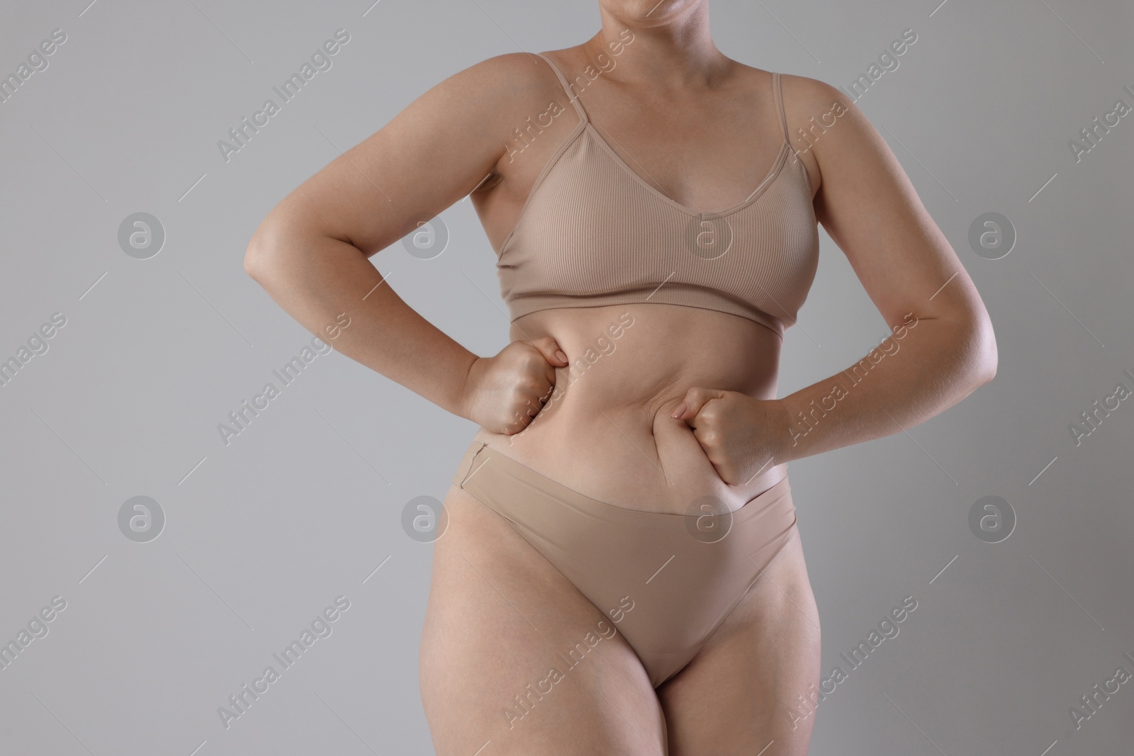 Photo of Liposuction. Woman in underwear touching her belly on grey background, closeup
