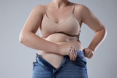 Photo of Liposuction. Woman trying to put on tight jeans against grey background, closeup