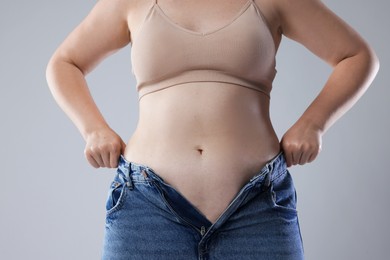 Photo of Liposuction. Woman trying to put on tight jeans against grey background, closeup
