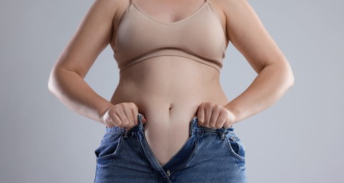 Photo of Liposuction. Woman trying to put on tight jeans against grey background, closeup