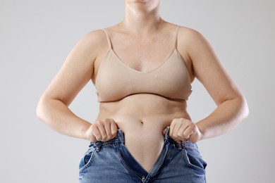 Photo of Liposuction. Woman trying to put on tight jeans against grey background, closeup