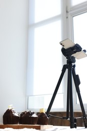 Photo of Shooting chocolate muffins with smartphone in studio, low angle view. Professional food photography