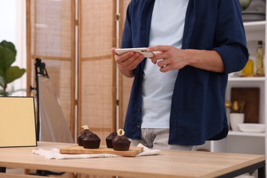Photo of Man taking picture of chocolate muffins in studio, closeup. Professional food photography
