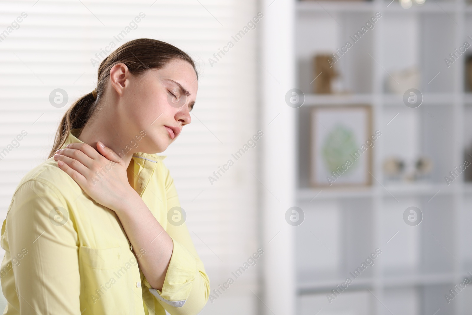 Young woman suffering from neck pain at home, space for text Photo of Young woman suffering from neck pain at home, space for text
