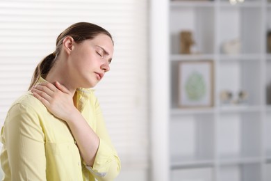 Photo of Young woman suffering from neck pain at home, space for text