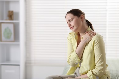 Photo of Young woman suffering from neck pain at home, space for text