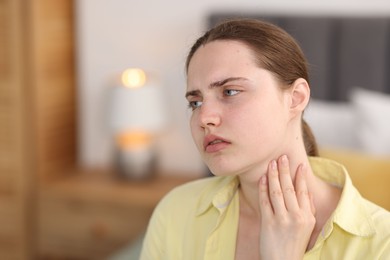 Photo of Young woman suffering from sore throat at home, space for text