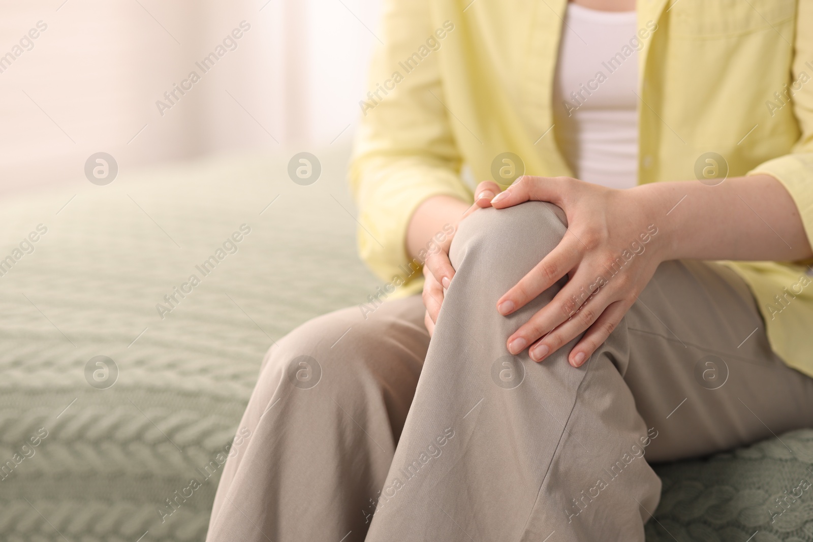 Photo of Young woman suffering from knee pain at home, closeup. Space for text
