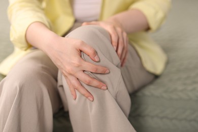 Photo of Young woman suffering from knee pain at home, closeup
