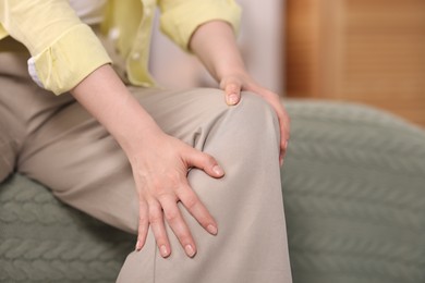 Photo of Young woman suffering from knee pain at home, closeup. Space for text
