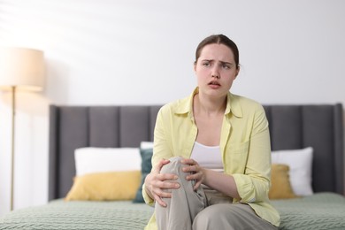 Photo of Young woman suffering from knee pain at home, space for text