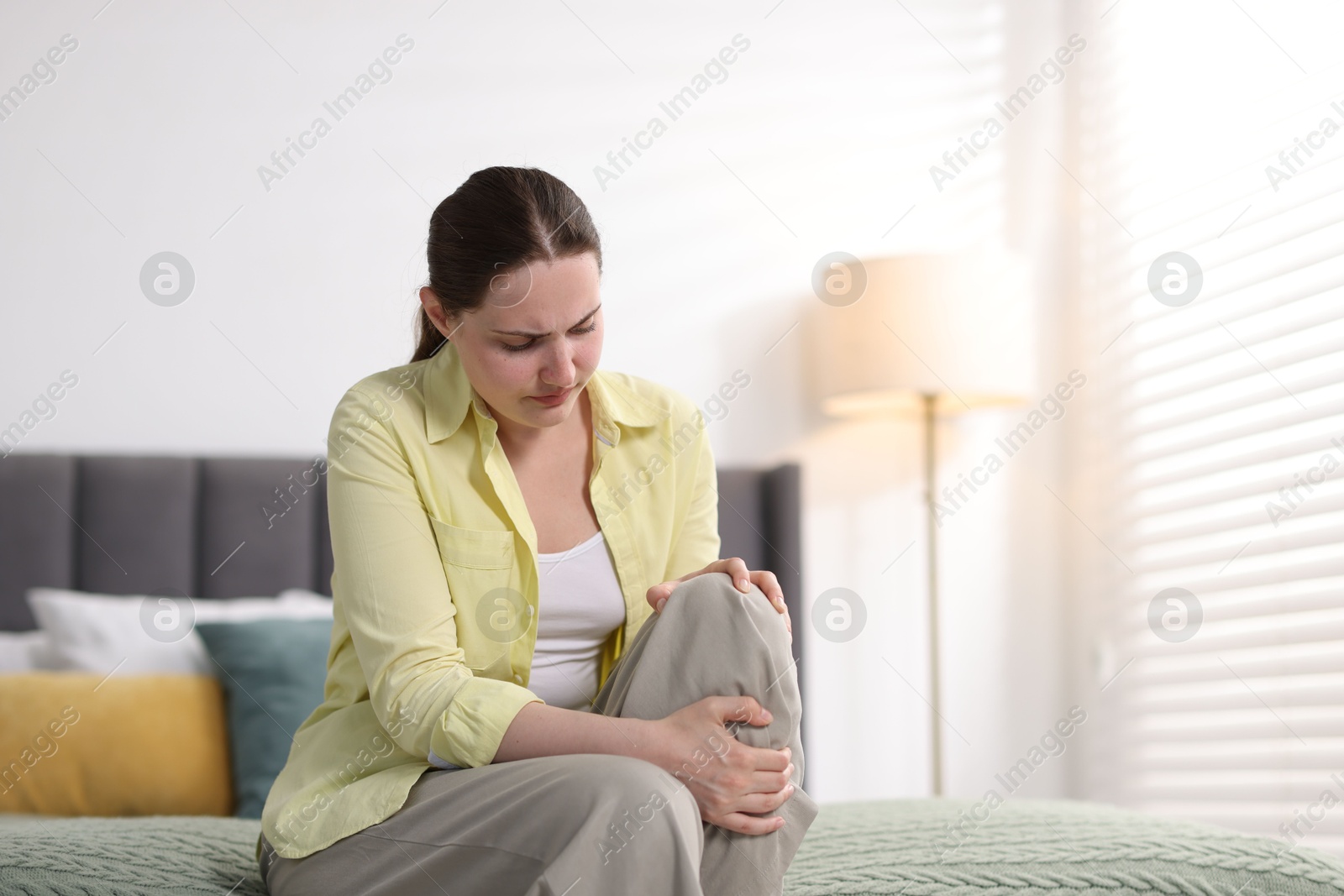 Photo of Young woman suffering from knee pain at home, space for text