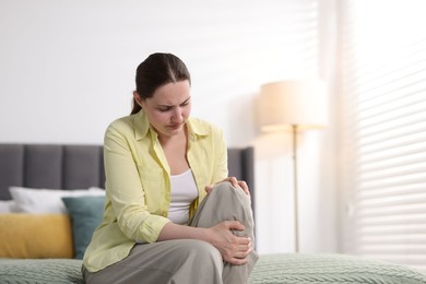 Photo of Young woman suffering from knee pain at home, space for text