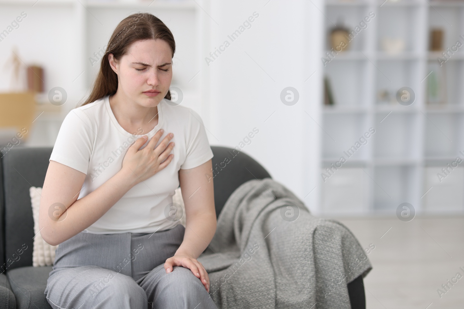 Photo of Young woman suffering from chest pain at home, space for text