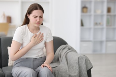 Photo of Young woman suffering from chest pain at home, space for text