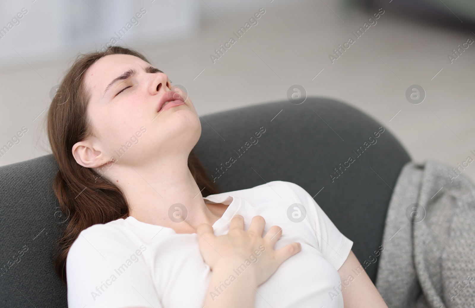 Photo of Young woman suffering from chest pain at home