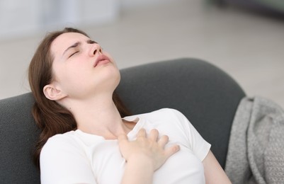 Photo of Young woman suffering from chest pain at home
