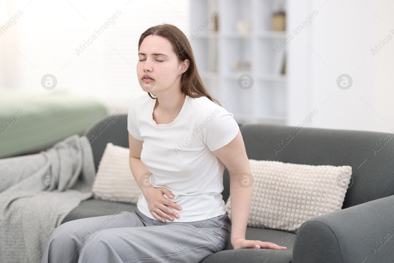 Photo of Young woman suffering from stomachache at home, space for text