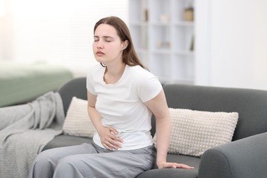 Photo of Young woman suffering from stomachache at home, space for text