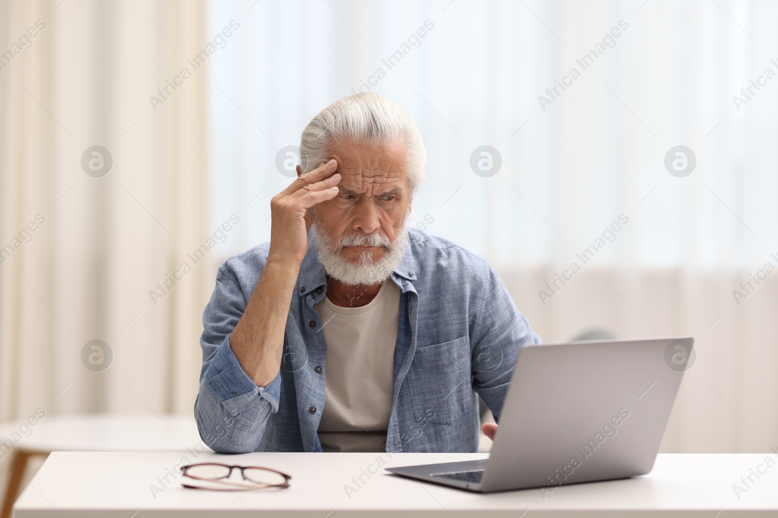Photo of Senior man suffering from headache at table indoors