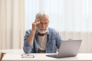 Photo of Senior man suffering from headache at table indoors