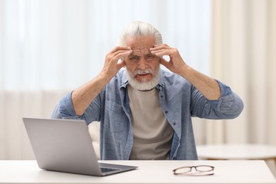 Photo of Senior man suffering from headache at table indoors
