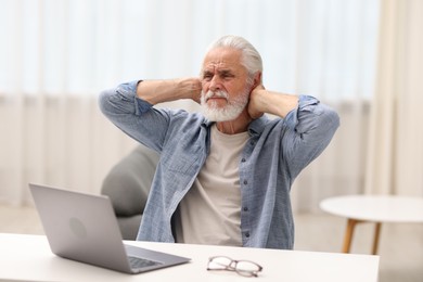 Photo of Senior man suffering from neck pain at table indoors
