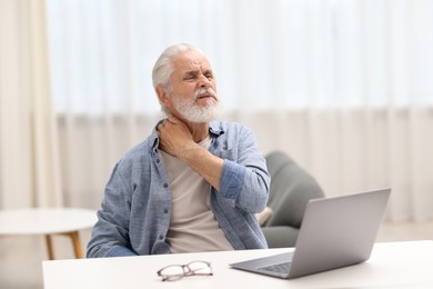 Photo of Senior man suffering from neck pain at table indoors