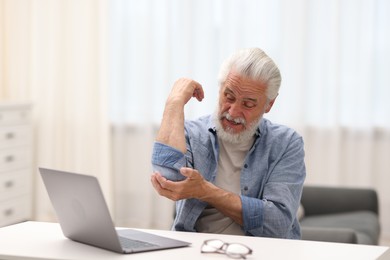 Photo of Senior man suffering from elbow pain at table indoors