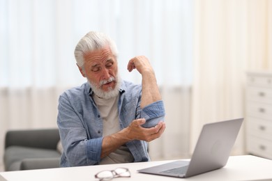 Photo of Senior man suffering from elbow pain at table indoors