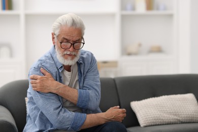 Photo of Senior man suffering from shoulder pain at home, space for text