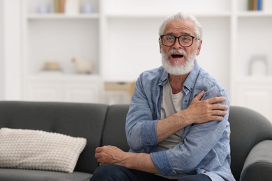 Photo of Senior man suffering from shoulder pain at home, space for text