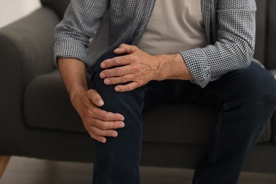 Photo of Senior man suffering from knee pain at home, closeup