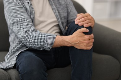 Photo of Senior man suffering from knee pain at home, closeup