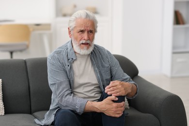 Photo of Senior man suffering from knee pain at home