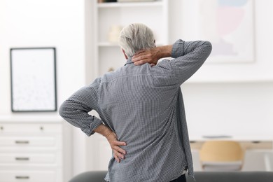 Photo of Senior man suffering from neck pain at home, back view