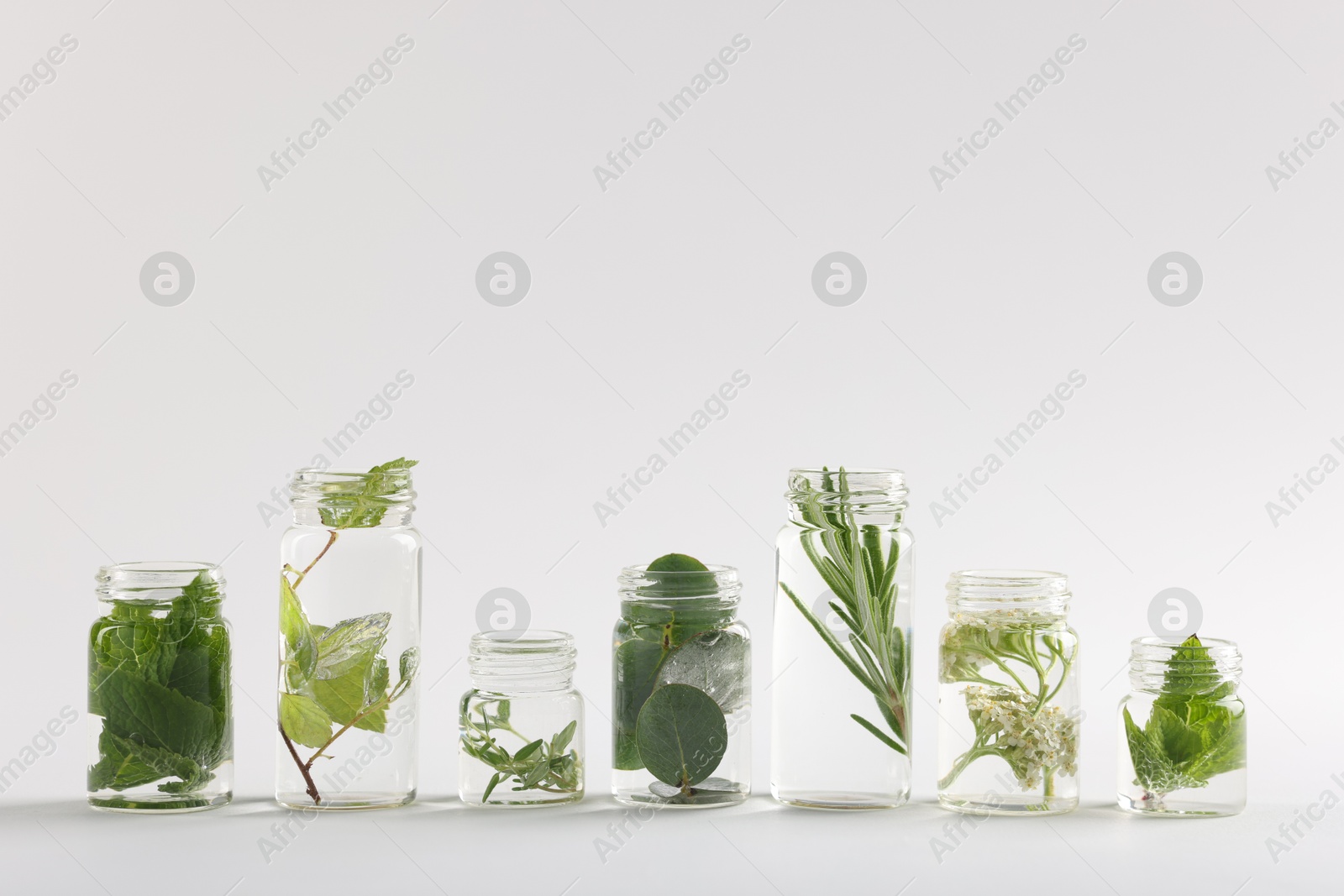 Photo of Essential oils with different plants in bottles on light grey background