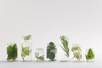 Photo of Essential oils with different plants in bottles on light grey background