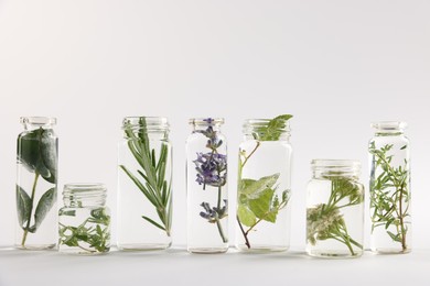 Photo of Essential oils with different plants in bottles on light grey background