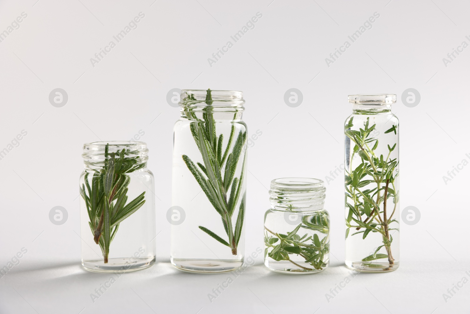 Photo of Essential oils with different plants in bottles on light grey background, closeup