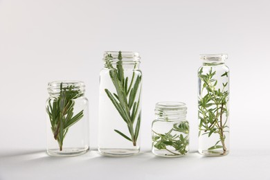 Photo of Essential oils with different plants in bottles on light grey background, closeup